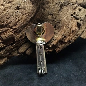 May include: A silver heart-shaped pendant with a gold circle in the center. The pendant is attached to a silver chain with a series of small, round holes.