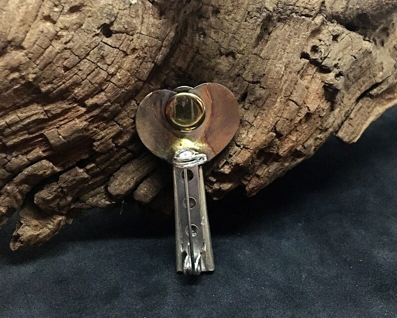 May include: A silver heart-shaped pendant with a gold circle in the center. The pendant is attached to a silver chain with a series of small, round holes.