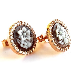 May include: A pair of gold-tone earrings with a white cameo flower design surrounded by clear rhinestones.