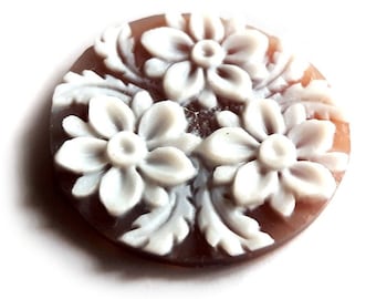Può includere: Un cammeo rotondo marrone con un motivo floreale bianco. Il cammeo presenta tre fiori intagliati con dettagli intricati.