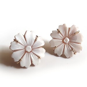 May include: A pair of white flower-shaped earrings with gold accents. The earrings are made of carved shell and have a delicate, feminine design.