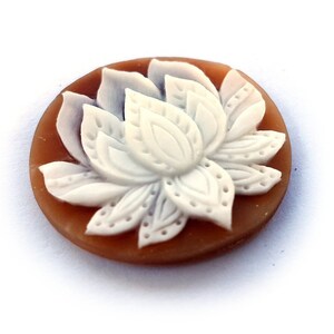Puede incluir: Un camafeo de concha marrón con un diseño de flor de loto tallada en blanco.