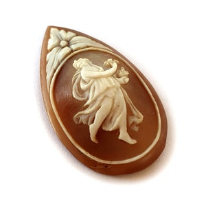 Puede incluir: Un colgante de camafeo marrón con una figura esculpida en blanco de una mujer sosteniendo una flor.