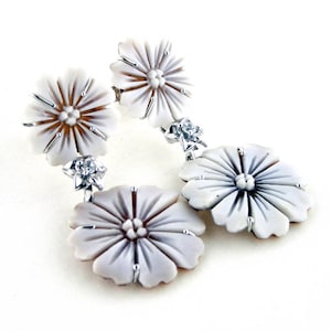 May include: Elegant floral earrings featuring white and gray flower designs with silver-tone accents and small, sparkling embellishments. The earrings have a drop style, showcasing detailed craftsmanship and a delicate aesthetic.