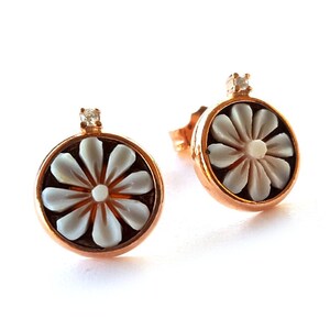 May include: A pair of gold-tone earrings with a white flower design and a small clear stone accent.