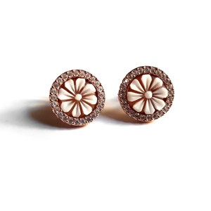 May include: A pair of rose gold stud earrings with a white flower design and clear crystal accents.