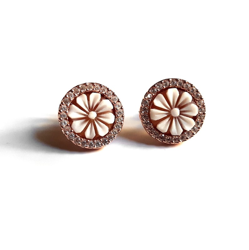 May include: A pair of rose gold stud earrings with a white flower design and clear crystal accents.