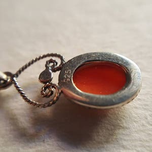 May include: Silver pendant with an orange cabochon stone set in a silver bezel. The back of the pendant has a silver bail and the inscription "925".