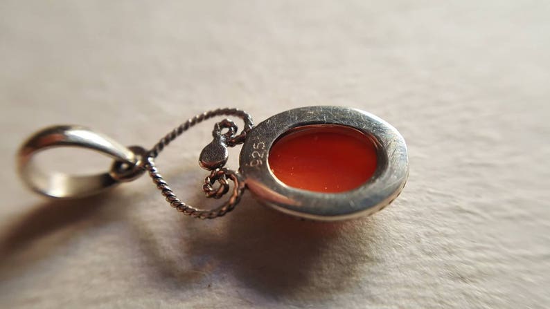 May include: Silver pendant with an orange cabochon stone set in a silver bezel. The back of the pendant has a silver bail and the inscription "925".