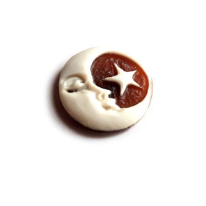 May include: A white ceramic button with a brown crescent moon and a white star design.