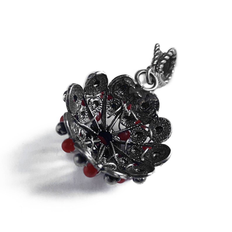 May include: A silver pendant with a filigree design and red beads. The pendant is shaped like a flower and has a loop at the top for attaching to a chain.