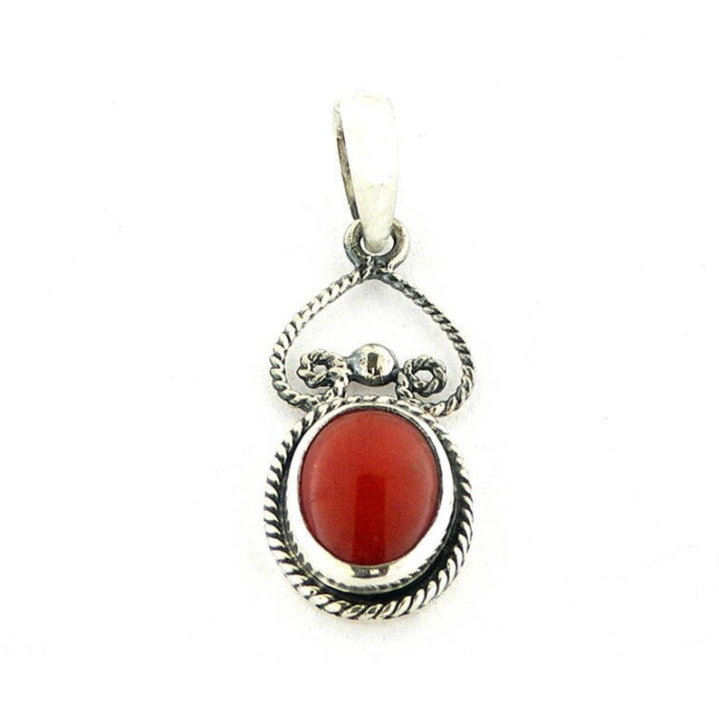 May include: A silver pendant with a red coral stone set in a decorative silver frame. The pendant has a bail for attaching to a chain.