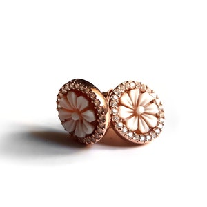 May include: A pair of rose gold earrings with a white flower design and a clear crystal halo.