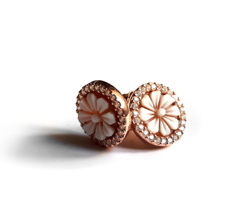 May include: A pair of rose gold earrings with a white flower design and a clear crystal halo.