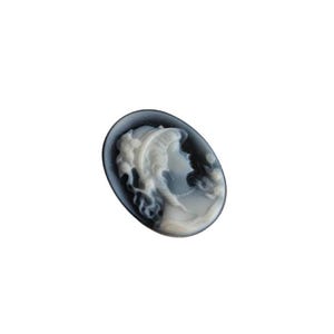 May include: Oval cameo pendant depicting a woman's profile with flowing hair and a pearl necklace. The cameo is carved in white against a dark grey background, set in a dark grey oval frame. A classic and elegant piece.