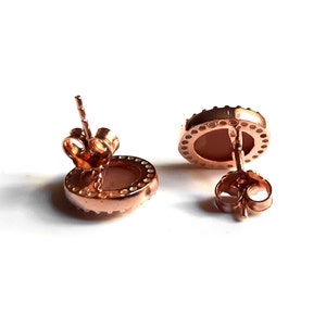 May include: A pair of rose gold stud earrings with a round, white stone set in a bezel setting. The earrings have a post and butterfly back.