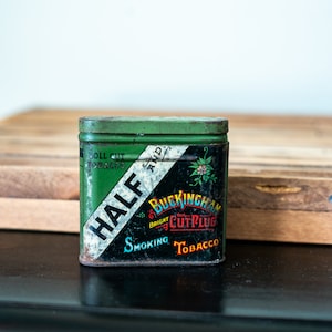May include: A green metal tin with a white label that reads "HALF" and "BUCKINGHAM BRIGHT CUT PLUG SMOKING TOBACCO".