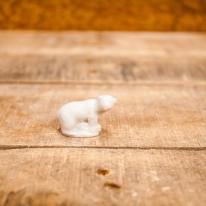 May include: A white porcelain figurine of a polar bear sitting on a wooden surface.
