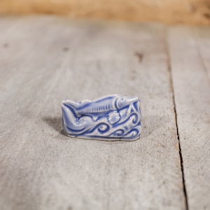 May include: A small blue and white ceramic figurine of a fish swimming in waves.