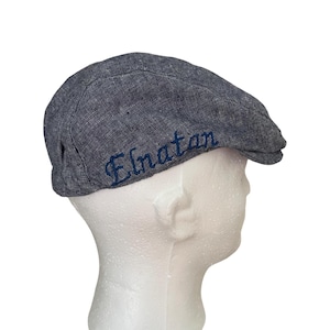 May include: A gray denim flat cap with a blue embroidered name "El'atan" on the side.