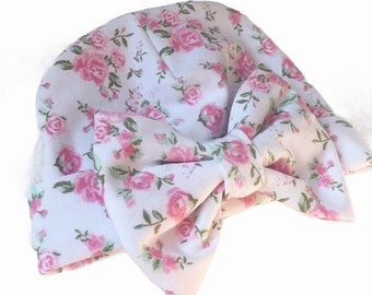 May include: A white baby hat with a pink floral pattern and a large bow tied on top.