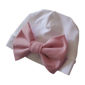 Op de afbeelding: Een witte muts met een grote roze strik aan de voorkant.