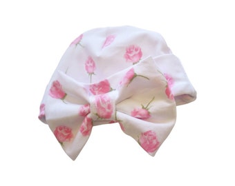 May include: White baby hat with a pink rose pattern and a large pink bow. The hat is made of soft cotton and is perfect for newborns and infants.