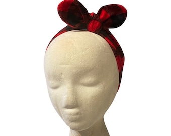 May include: Red and black plaid headband with a bow on top. The headband is tied in a knot at the back of the head.