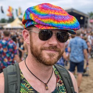 Peut inclure: Casquette de style gavroche tie-dye aux couleurs de l'arc-en-ciel. La personne porte des lunettes de soleil aviateur et un collier. La personne se trouve dans une foule lors d'un événement en plein air.