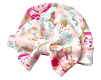 May include: A pink and white floral print baby hat with a large bow on top. The hat is made of soft cotton and is perfect for keeping a baby's head warm.