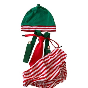 Puede incluir: Un conjunto de elfo navideño para bebé, que incluye un gorro verde con rayas rojas y blancas, un pañal con rayas rojas y blancas, una corbata roja y tirantes verdes.