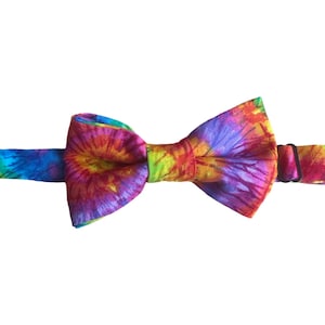 May include: A tie-dye bow tie with a rainbow colour pattern. The bow tie is made of fabric and has a black adjustable strap.