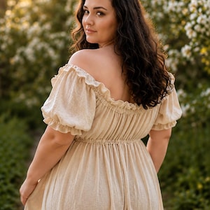 May include: A beige off-the-shoulder dress featuring short puff sleeves with ruffled edges, a gathered elasticized neckline, and a cinched elastic waistline. The garment is crafted from a textured fabric and falls into a flowing skirt.