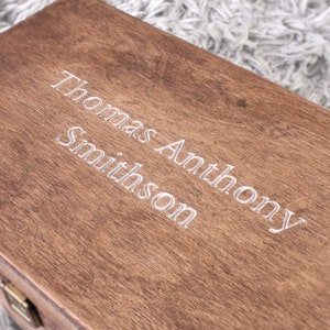 K&ouml;nnte beinhalten: Eine Holzkiste mit dem eingravierten Namen "Thomas Anthony Smithson" auf der Oberseite.
