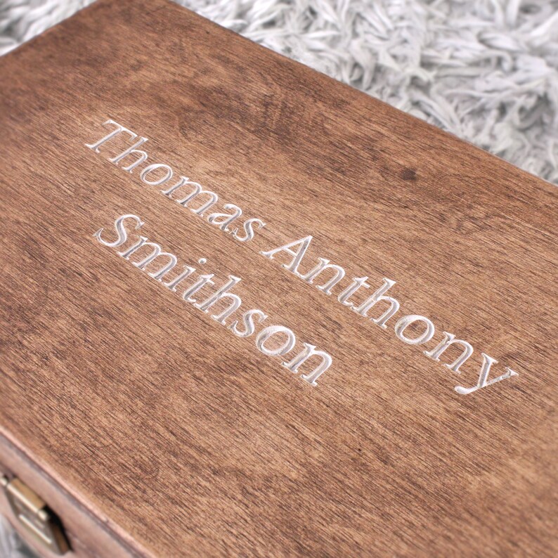 K&ouml;nnte beinhalten: Eine Holzkiste mit dem eingravierten Namen "Thomas Anthony Smithson" auf der Oberseite.
