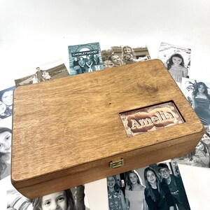 May include: A wooden box with a copper plaque engraved with the name "Amelia". The box is surrounded by photographs.