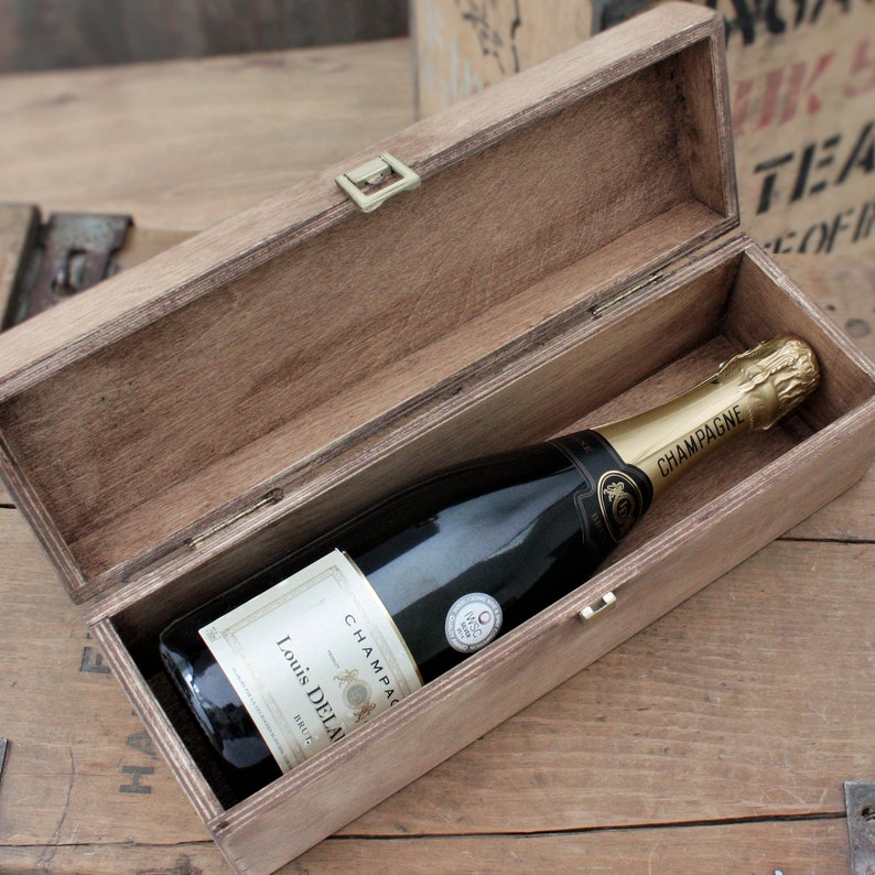 Puede incluir: Una caja de madera con tapa abatible, abierta para revelar una botella de champ&aacute;n. La botella est&aacute; etiquetada con "Louis Delaunay" y "Champagne".