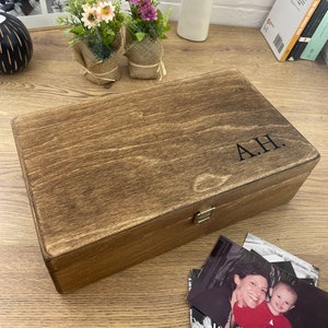 May include: A wooden box with a hinged lid and a brass latch. The box is stained a dark brown colour and has the initials "A.H." engraved on the top.