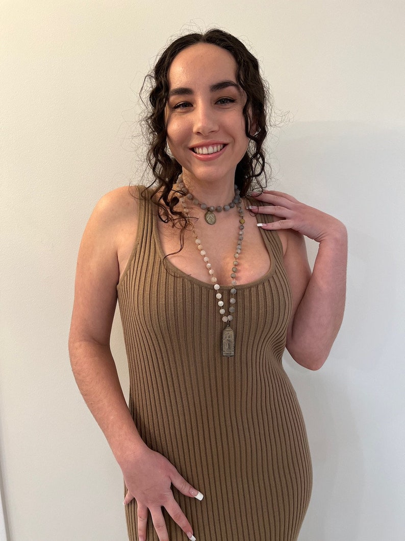 May include: A woman wearing a brown ribbed sleeveless dress with a long beaded necklace featuring a silver pendant.