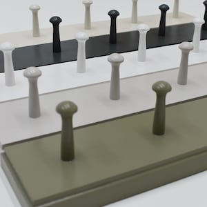 May include: A set of wooden wall hooks with different coloured knobs. The hooks are arranged in a staggered pattern, with the knobs facing forward. The knobs are in the colours black, white, grey, light brown, and green.
