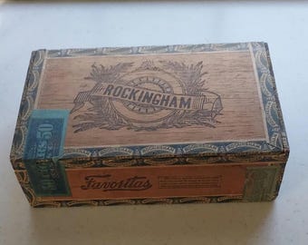 May include: Rectangular wooden box with the word "ROCKINGHAM" in a banner across the top. The box has a light brown color with a blue and brown border. The word "Favoritas" is printed on the front.