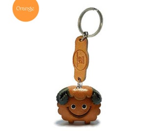 Pode incluir: Um chaveiro de couro castanho com um amuleto de ovelha de desenho animado. A ovelha tem orelhas verdes e uma cara sorridente. O chaveiro tem um aro de chave prateado e uma etiqueta de couro castanho com o texto "TZ" nele.