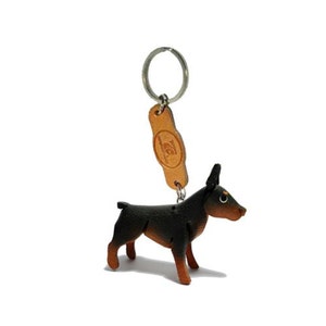 May include: A black and tan leather Doberman Pinscher keyring with a brown leather tag that says "Leather Crafts" and a silver key ring.