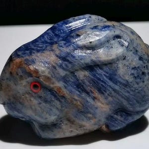 May include: A blue and white carved stone rabbit figurine with a red eye. The rabbit is made of a type of stone with a swirling pattern.