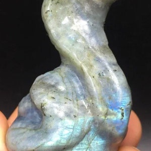 May include: A carved labradorite stone sculpture of a snake. The stone is iridescent with shades of blue, green, and gray.