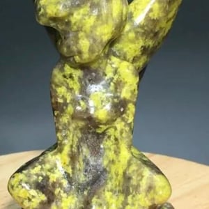 Puede incluir: Una pequeña figurita de ángel sentada con alas, de color amarillo y negro. La figurita está hecha de piedra natural con un patrón moteado.