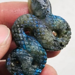 May include: A carved labradorite snake pendant with a blue and green iridescent sheen. The snake is coiled in a figure eight shape.