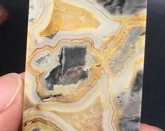May include: A polished, irregularly shaped slab of agate with a unique pattern of gray, white, and yellow bands. The agate has a natural, organic look and feel.