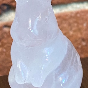 May include: A translucent, carved crystal rabbit figurine. The bunny is in a seated position with its ears upright. The crystal has a subtle iridescent quality, catching the light. The figurine is a decorative item, likely for display.