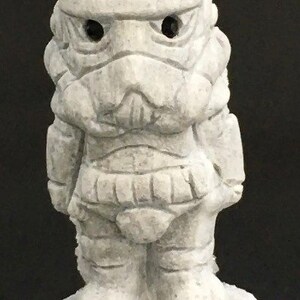 May include: A white ceramic figurine of a Star Wars Stormtrooper. The figurine is detailed with a textured surface and has a black base.